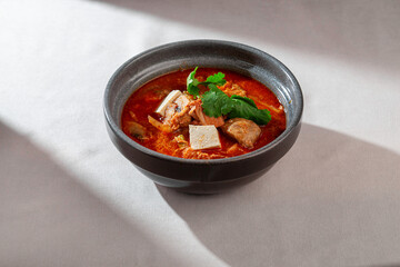 A rich and vibrant bowl of traditional Korean Kimchi Jjigae soup, featuring tender tofu, savory mushrooms, and fresh cilantro garnish