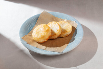 Three perfectly golden-brown, fluffy pancakes or syrniki, freshly cooked and served on a piece of parchment paper on a light blue plate