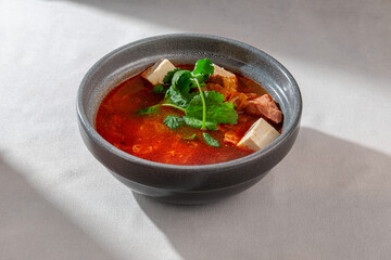 A vibrant and appetizing bowl of Asian-inspired Kimchi soup, rich with red broth, tender tofu, savory meat, and a fresh cilantro garnish