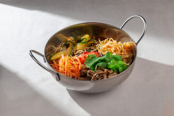 A colorful and inviting Asian noodle bowl, generously filled with tender meat, fresh vegetables, and topped with vibrant cilantro and sesame seeds, served in a metal pot