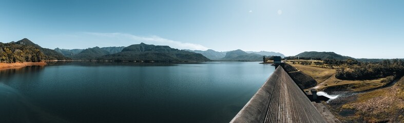 Obraz premium Paisagem Panorâmica de Barragem com Lago e Montanhas em Dia Ensolarado