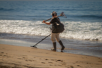 A man using a metal detector on a beach with the ocean and waves in the background