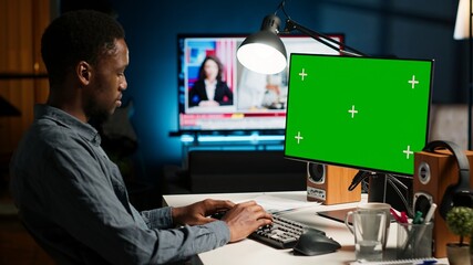 African american adult working from home using chroma key mockup, reviewing statistical data to compare supply and demand numbers. Sitting at desk and writing on his computer. Camera B.