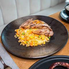 Asian Fusion Dish with Grilled Meat and Vegetable Rice on a Black Plate