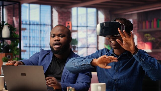 African American woman explores virtual reality using a VR headset while her partner works remotely on a laptop. Young couple embraces modern technology and gadgets with AI at home. Camera B.