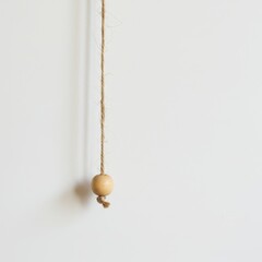 Hanging wooden bead on natural twine against a white wall.