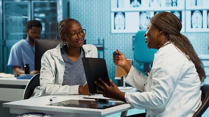Female doctor using clinical scans and records to advise a patient during routine checkup, focusing on treatment and medical expertise. Specialist expert advising young girl. Camera A.