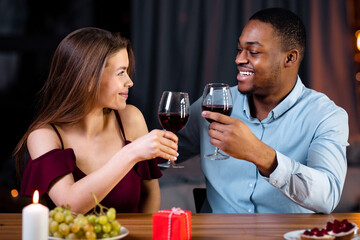 Affectionate Mixed Couple Having Romantic Dinner In Restaurant, Drinking Red Wine And Smiling. Young Interracial Lovers Celebrating Anniversary Or Valentine's Day Together In Elegant Atmosphere