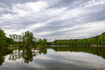Landscape with forest lake, trees and sky covered with rain clouds. Forest lake in cloudy weather.