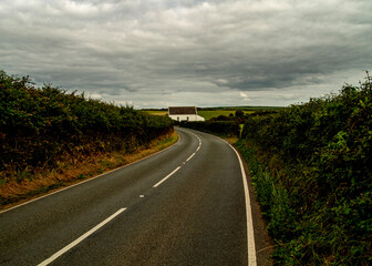 A winding road leads towards a white building under a cloudy sky.