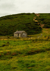 Obraz premium A stone building sits in a grassy field, with a path leading up a hill in the background.