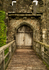 Naklejka premium A wooden bridge leading to a large wooden door in a stone castle.
