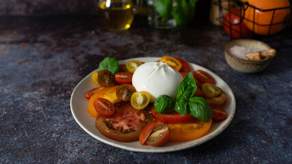 Front view close up of colorful sliced tomatoes with burrata in center, fresh basil, olive oil...