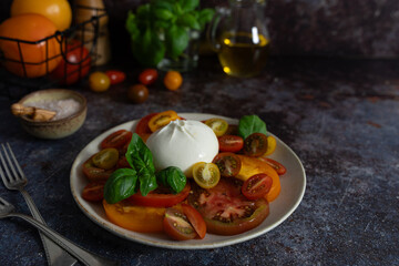 Front view of burrata surrounded by colorful tomatoes, fresh basil, olive oil bottle and sea salt...