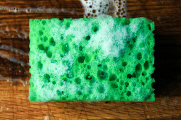 green kitchen cleaning sponge with foam on wooden table
