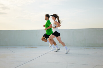 Dynamic couple jogging on modern rooftop during their fitness routine and enjoying the fresh air while building endurance and strength together