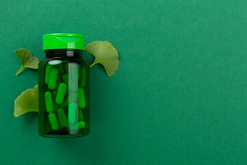 Ginkgo leaf with bottle of pills on color background, top view