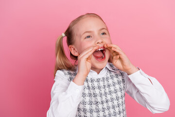Joyful schoolgirl with pigtails shouting cheerfully against a pink background, wearing a formal school uniform