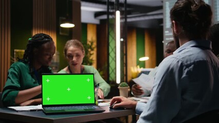 Diverse project team meeting after hours next to mockup display, sharing data visualization reports to discuss business intel. Forecasts for upcoming presentation to investors group. Camera A. - Powered by Adobe