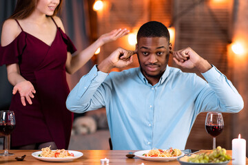 Interracial Couple Arguing. Young Multicultural Lovers Having Conflict During Date In Restaurant, Annoyed Black Man Closing Ears With Fingers, Ignoring His Complaining Girlfriend, Free Space