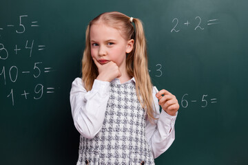 Portrait of a young schoolgirl in formal attire holding chalk against a chalkboard displaying math equation