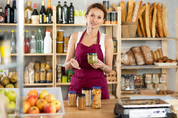 Portrait of female seller offering to buy canned green peas and beans in supermarket