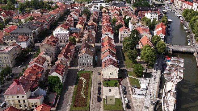 Aerial perspective of Klaipėda Old Town, Lithuania, featuring narrow streets, historic red-roofed buildings, landscaped public spaces, and a docked sailing ship along the riverfront.