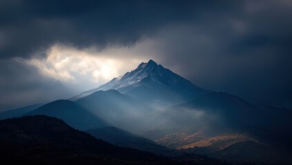 Mountain peak bathed in sunlight piercing dark clouds