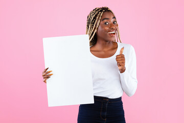 Cheerful Black Woman Showing Thumbs Up Sign Gesture And Holding Blank Paper Poster For Your Text Smiling To Camera Standing Over Pink Studio Background. Lady With White Vertical Board For Advertising
