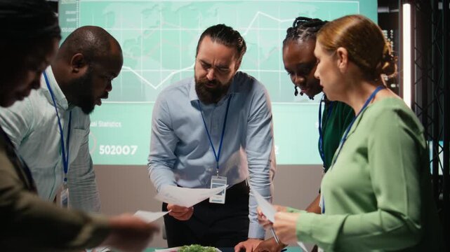 Diverse group of professionals review files and performance metrics, using projections and budgeting to align the company goals with stakeholder expectations for company progress. Camera A.