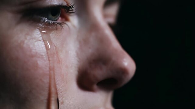 A tear drop glistening on a female cheek, slowly rolling downwards, powerfully conveys raw human emotion, sadness, and vulnerability in a moment of quiet grief.