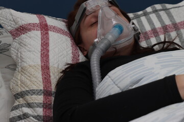 Adulto young woman sleeping with a cpap mask to treat a apnea disorder while wearing a black clothes