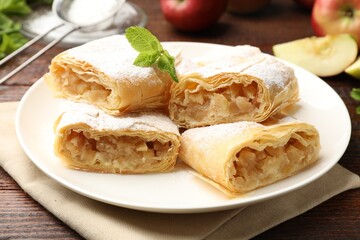 Pieces of tasty apple strudel with powdered sugar and mint on wooden table, closeup