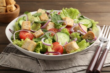Delicious salad with croutons and vegetables served on wooden table, closeup