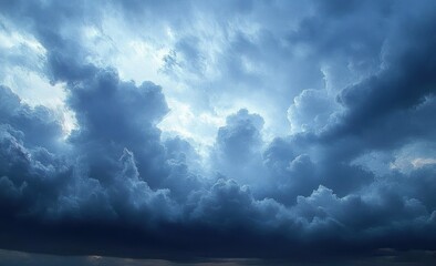 Obraz premium Dramatic and dense dark blue storm clouds covering the sky with patches of light shining through creating a mysterious and intense mood