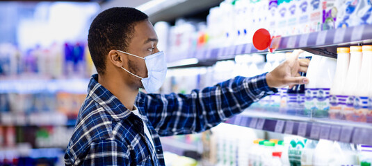 Side view of African American man in face mask choosing dairy products at supermarket during...