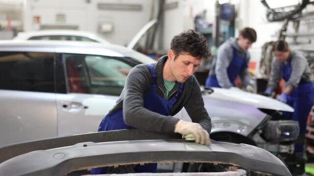 Car bumper repair in car service - professional car painter polishes and prepares the bumper before painting. High quality 4k footage