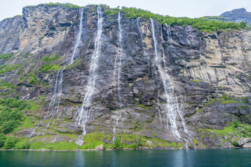Flush on view of the massive Seven Sisters waterfall in the UNESCO landmark lush green tree-lined fjord named Geirangerfjord, in the Nordic village, Geiranger, Norway in day