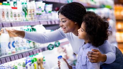 Positive black mom with her child shopping for products at dairy section of mall. Cheerful African...
