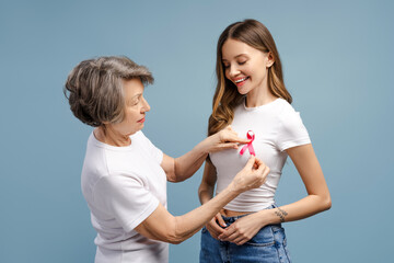 Senior woman attaching pink ribbon on young woman's t-shirt: breast cancer awareness