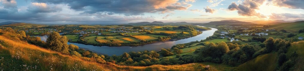 Obraz premium Scenic panoramic view of a winding river flowing through green fields and scattered houses during a golden sunset with dramatic clouds and distant hills