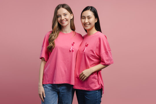 Two smiling women wearing pink ribbon showing support for breast cancer awareness