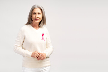 Senior smiling woman wearing white sweater with pink ribbon looking at camera on white background