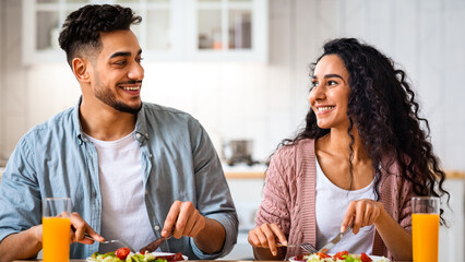 Romantic middle-eastern couple having healthy breakfast together in kitchen at home, happy arab man and woman eating delecious meal, drinking orange juice and looking at each other, closeup
