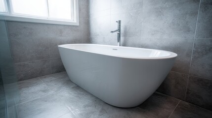 Modern, oval-shaped bathtub in a gray tiled bathroom.