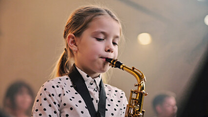 Young Musician with Saxophone: A young girl intently plays a saxophone, showcasing her musical talent and dedication in a performance setting.