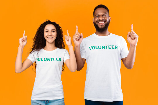 Look There. Female And Male Volunteers Couple Pointing Fingers Up Advertising And Recommending Something Posing Over Yellow Studio Background. Volunteering And Charity Advertisement Concept - Powered by Adobe