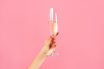 Closeup of female hand holding glass of champagne on pink studio background. Unrecognizable young lady having fun party, celebrating holiday with alcoholic drink, toasting and cheering
