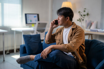 A man is sitting on a blue couch and talking on his cell phone