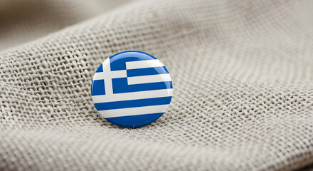 Small, round, Greek flag button pinned to a beige fabric.